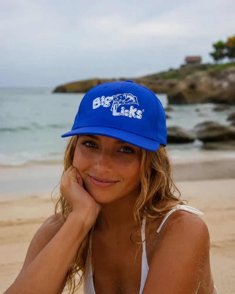A woman wearing the royal blue Big Licks cap on the beach